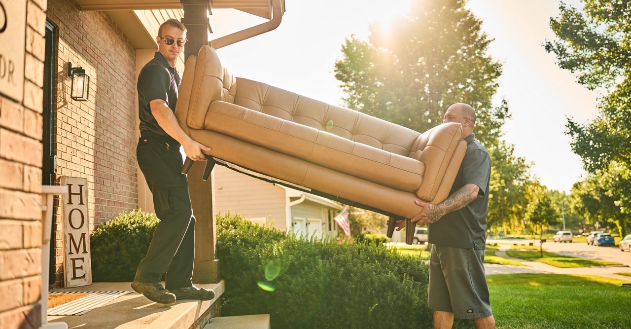 two in-home delivery team members carrying a sofa inside a home
